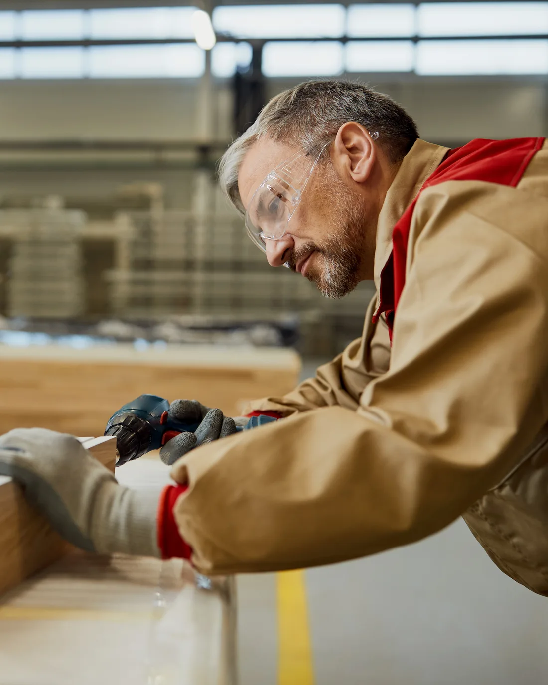 Tischler mit Schutzbrille arbeitet in einer hellen Werkstatt konzentriert an der Kante eines Werkstücks