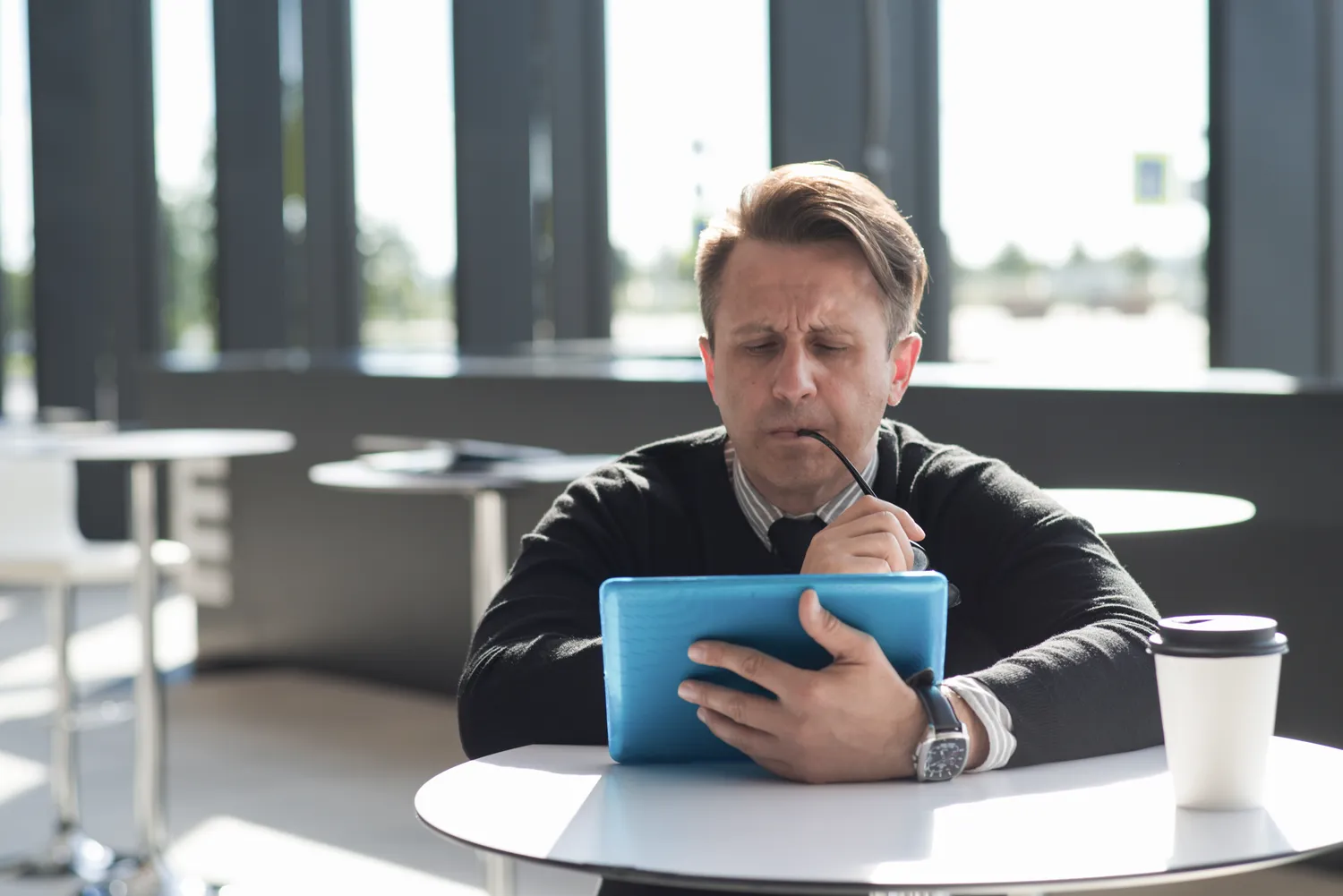 Unternehmer sitzt mit Kaffee an einem Tisch und schaut skeptisch auf die Webseite auf seinem Tablet